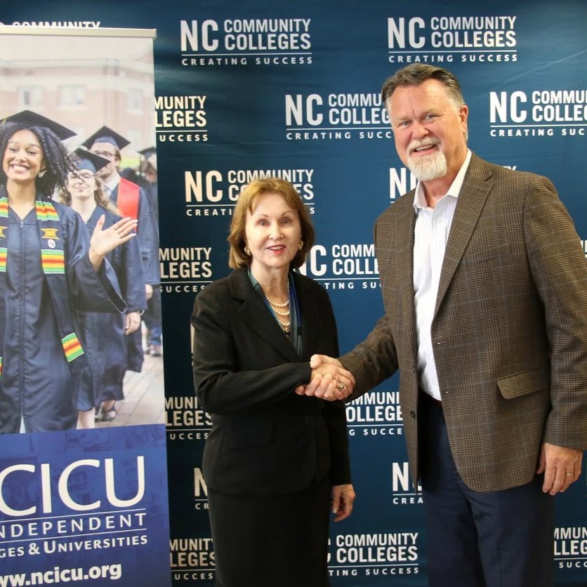 A woman and man shake hands in front of banners representing NC Independent Colleges & Universities and the NC Community College System.